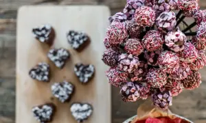 En bukett med rosa och lila cake pops, dekorerade med strössel och hjärtan. Bredvid ligger mörka hjärtformade cake pops.