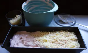 Förberedelser för ett gott kassler recept: en form med kassler och ost, en skål med riven ost och en tom blandskål.