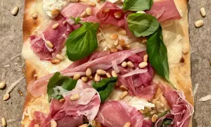 En läcker pinsa bianco med tunt skivad prosciutto, pinjenötter, färsk basilika och krämig ost.