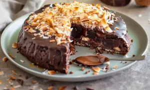 Kladdkaka med kokostosca, chokladig och härlig, toppad med rostad kokos. En sked med chokladsås väntar.
