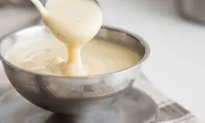 Krämig vaniljsås hälls från en slev i en skål. Perfekt för ditt vaniljsås recept.