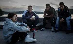 Fyra unga män sitter vid vattnet i skymningen, en scen från filmen Vinterviken (2021).