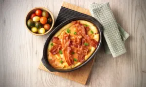 En härlig ugnspannkaka med knaprigt bacon och färska örter, serverad med en skål körsbärstomater.