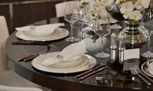 Elegant dukning med bestick, en vit servett med silverring och glas. En vacker blomsteruppsättning pryder bordet.