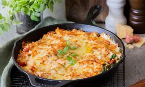 En gyllene, bubblande vegetarisk lasagne i gjutjärnspanna, toppad med färska örter. Perfekt för en mysig middag.