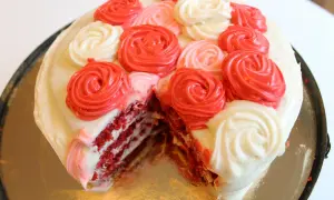 En skivad red velvet cake med vit frosting och dekorationer i form av röda och rosa rosor.