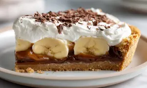 En bit krämig banoffee paj med lager av banan, kolasås och vispad grädde, toppad med chokladspån.