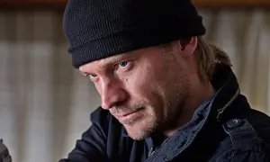 En man med svart mössa och skäggstubb, kanske en karaktär från filmer och tv-program med Jo Nesbø.