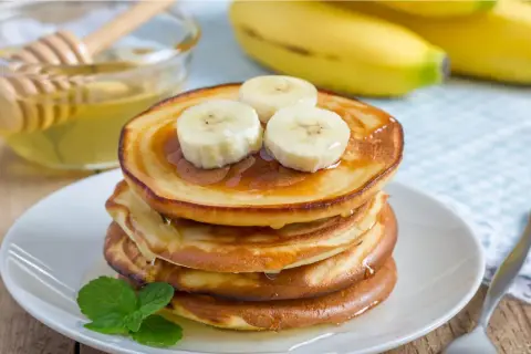 En stapel fluffiga bananpannkakor toppade med bananskivor och honung. Ett perfekt bananpannkaka recept för en härlig frukost.