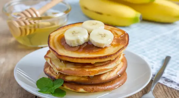 En stapel fluffiga bananpannkakor toppade med bananskivor och honung. Ett perfekt bananpannkaka recept för en härlig frukost.