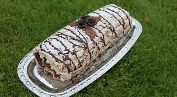 En läcker Budapestrulle med chokladrosor och pudersocker, redo att avnjutas. Ett perfekt recept för fika.