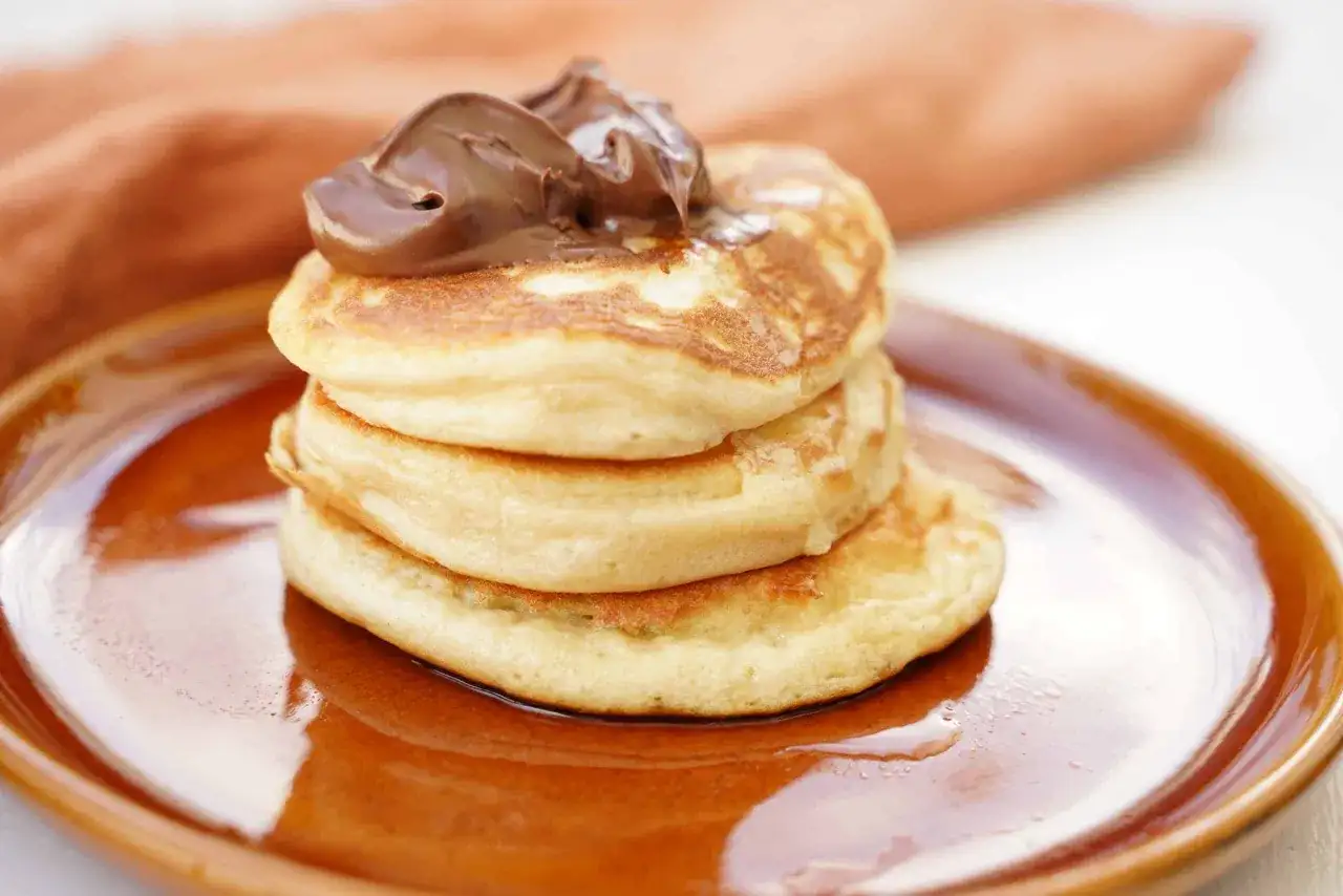 En stapel fluffiga amerikanska pannkakor med chokladkräm på toppen, serverade på en brun tallrik.