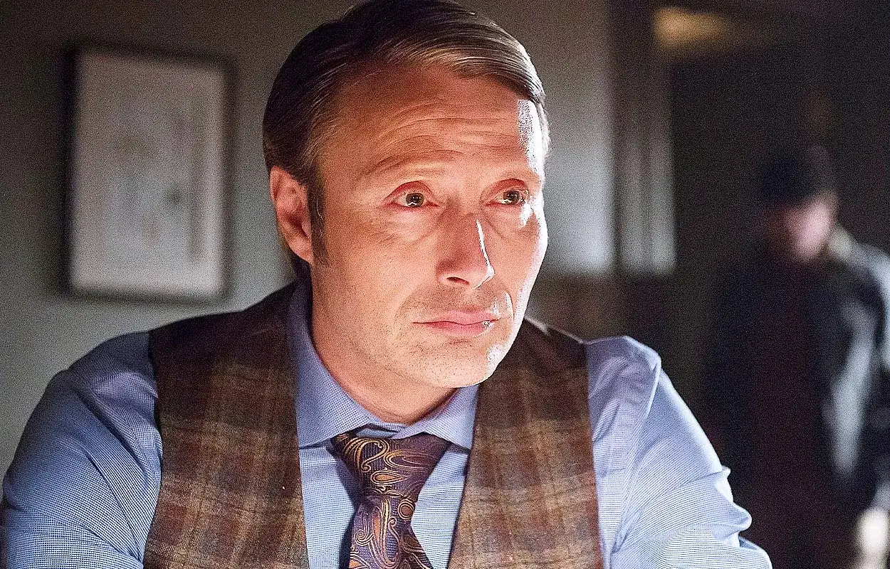 Mads Mikkelsen i en rutig väst och mönstrad slips, en ikonisk karaktär från filmer och tv-program.