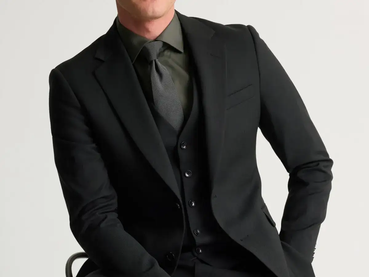 Man i svart kostym med grå skjorta och slips. En stilren outfit som passar bra för en fluga på begravning.