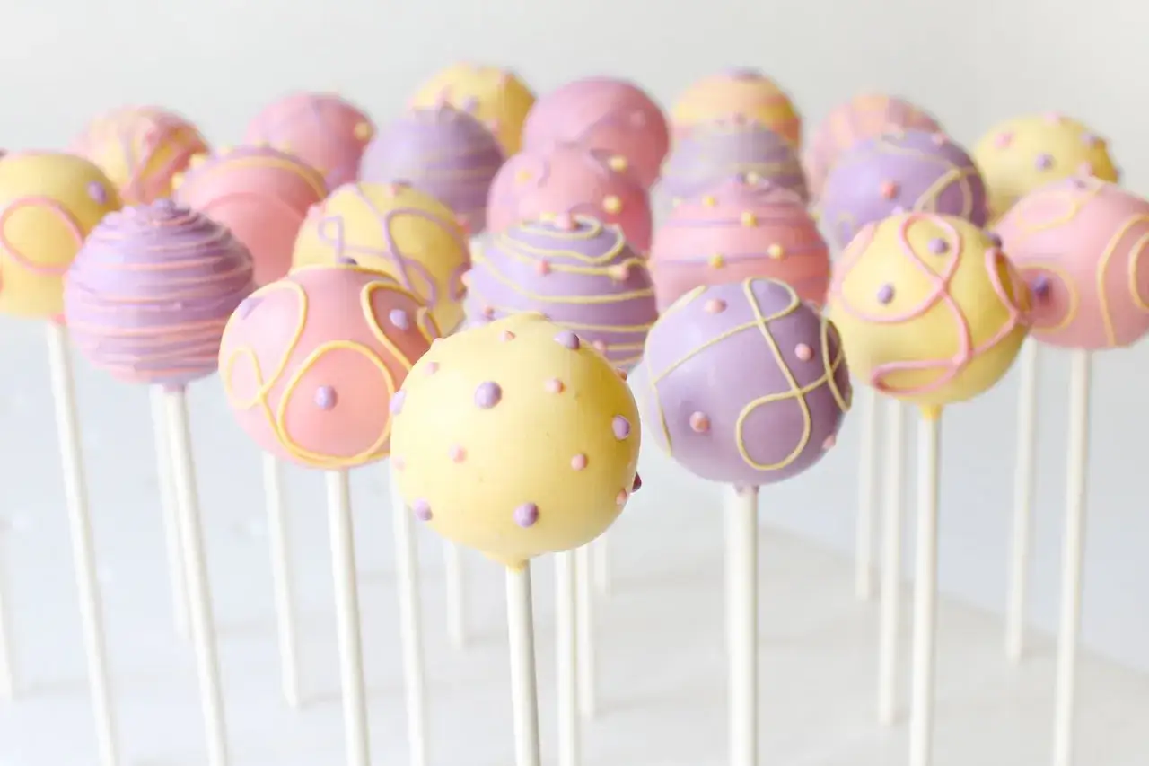 En samling färgglada cake pops i pastellfärger, dekorerade med mönster och prickar. Perfekta för ett festligt kalas!