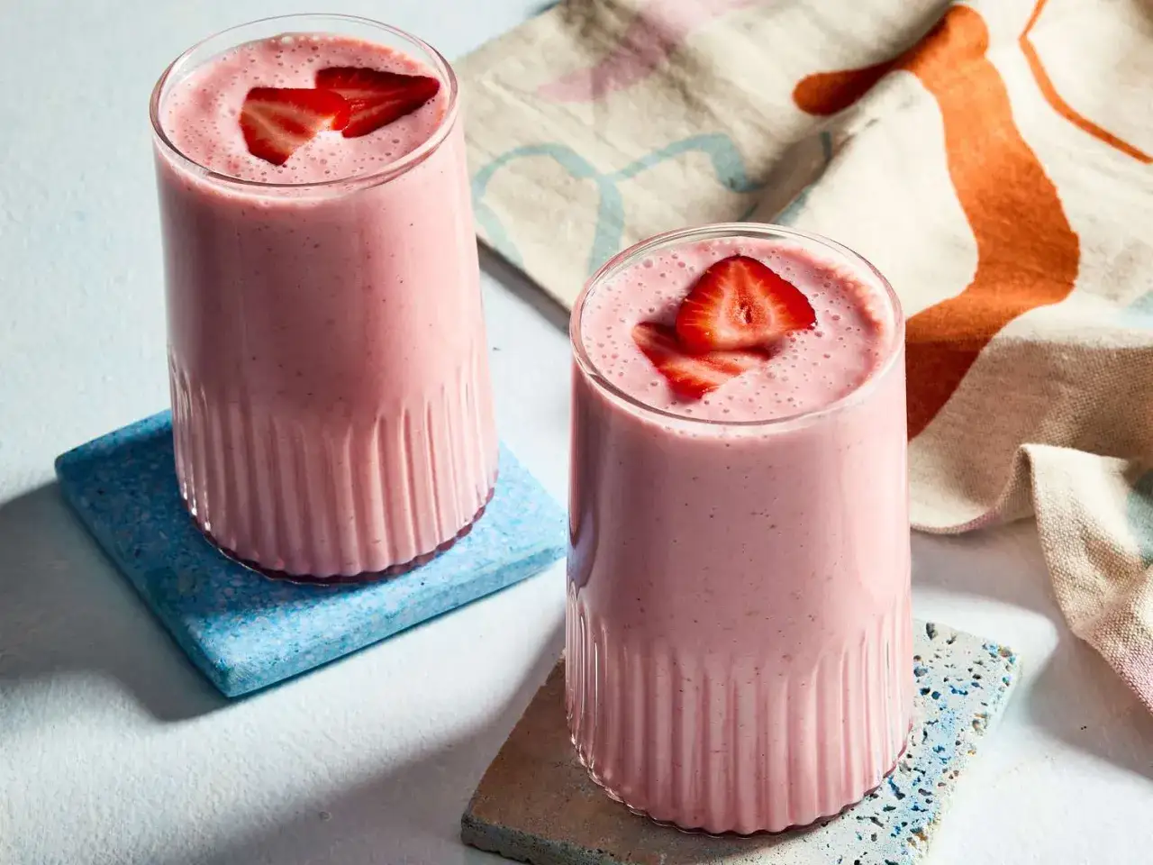 Två glas med rosa jordgubbssmoothie, toppade med färska jordgubbar. Ett perfekt smoothie recept för en solig dag.
