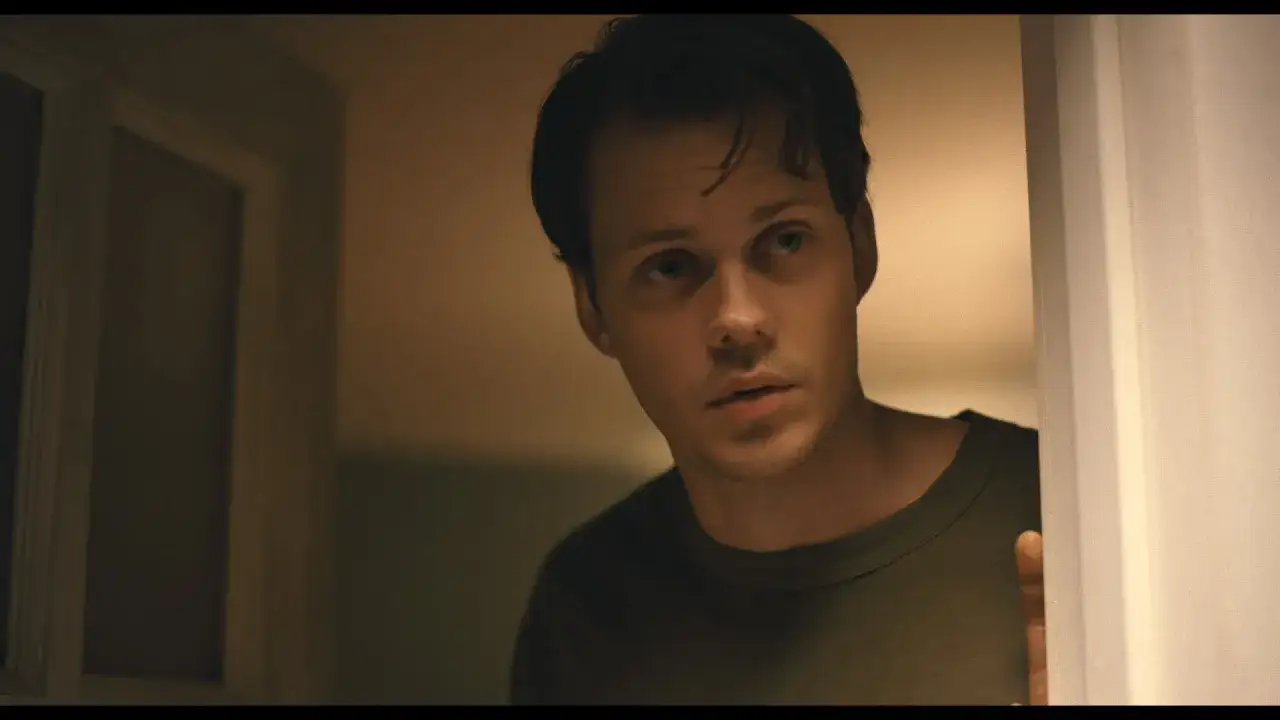 Bill Skarsgård kikar fram bakom en dörr, med en fundersam blick.