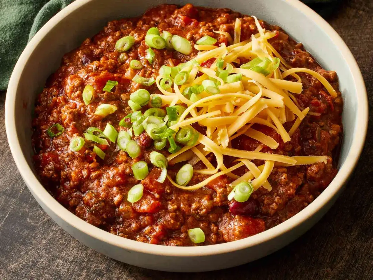 En skål med mustig chili con carne, toppad med riven ost och färsk salladslök. Perfekt för en kall kväll!