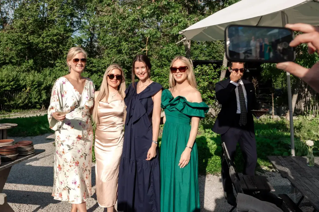 Fyra personer i formell klädsel poserar utomhus. En man tar bild med mobil.