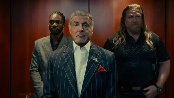Sylvester Stallone i en serie, flankerad av två män i en hiss.