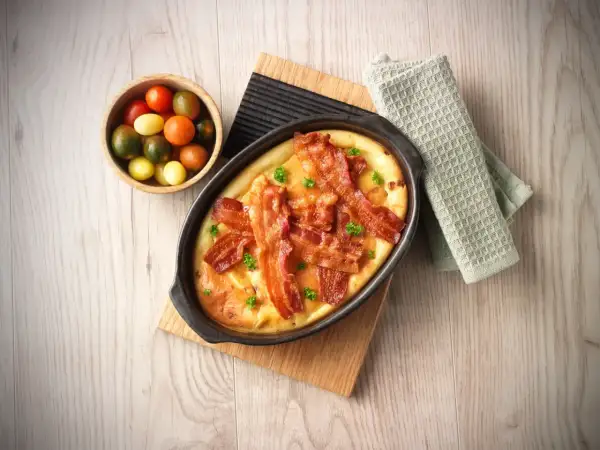 En härlig ugnspannkaka med knaprigt bacon och färska örter, serverad med en skål körsbärstomater.