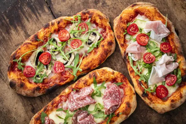 Tre läckra pinsor med salami, prosciutto, tomater och ruccola på en träbakgrund. Ett perfekt pinsa recept för en mysig kväll.