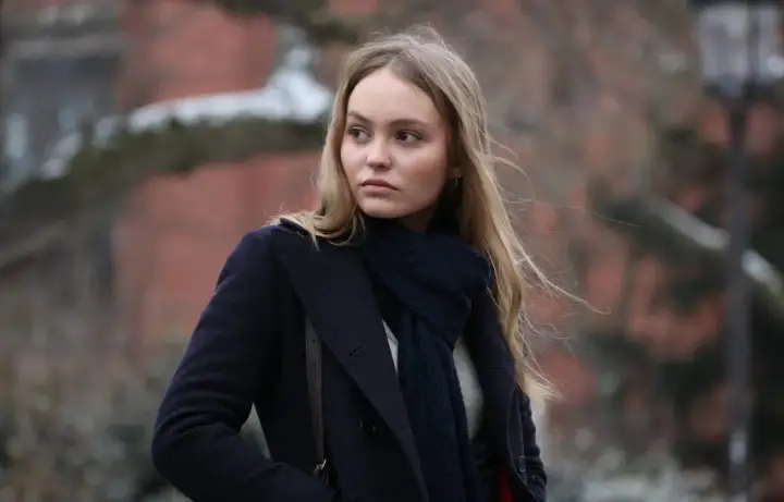 Lily-Rose Depp i en mörkblå kappa och halsduk, påminner om hennes roller i filmer.